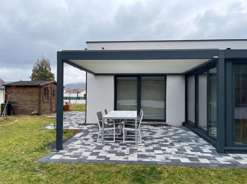 Terrasse extérieure moderne avec pergola bioclimatique à lames orientables en aluminium anthracite, fixée en appui mural