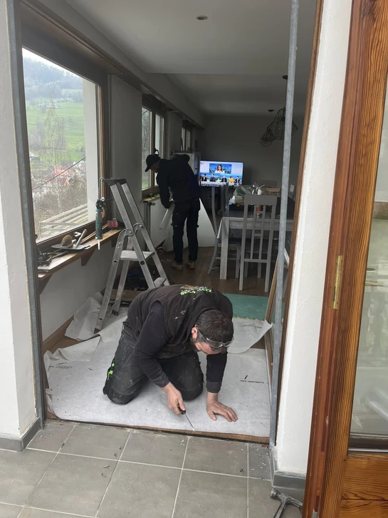 Vue intérieure d'une véranda donnant sur un jardin verdoyant avec arbres de conifères