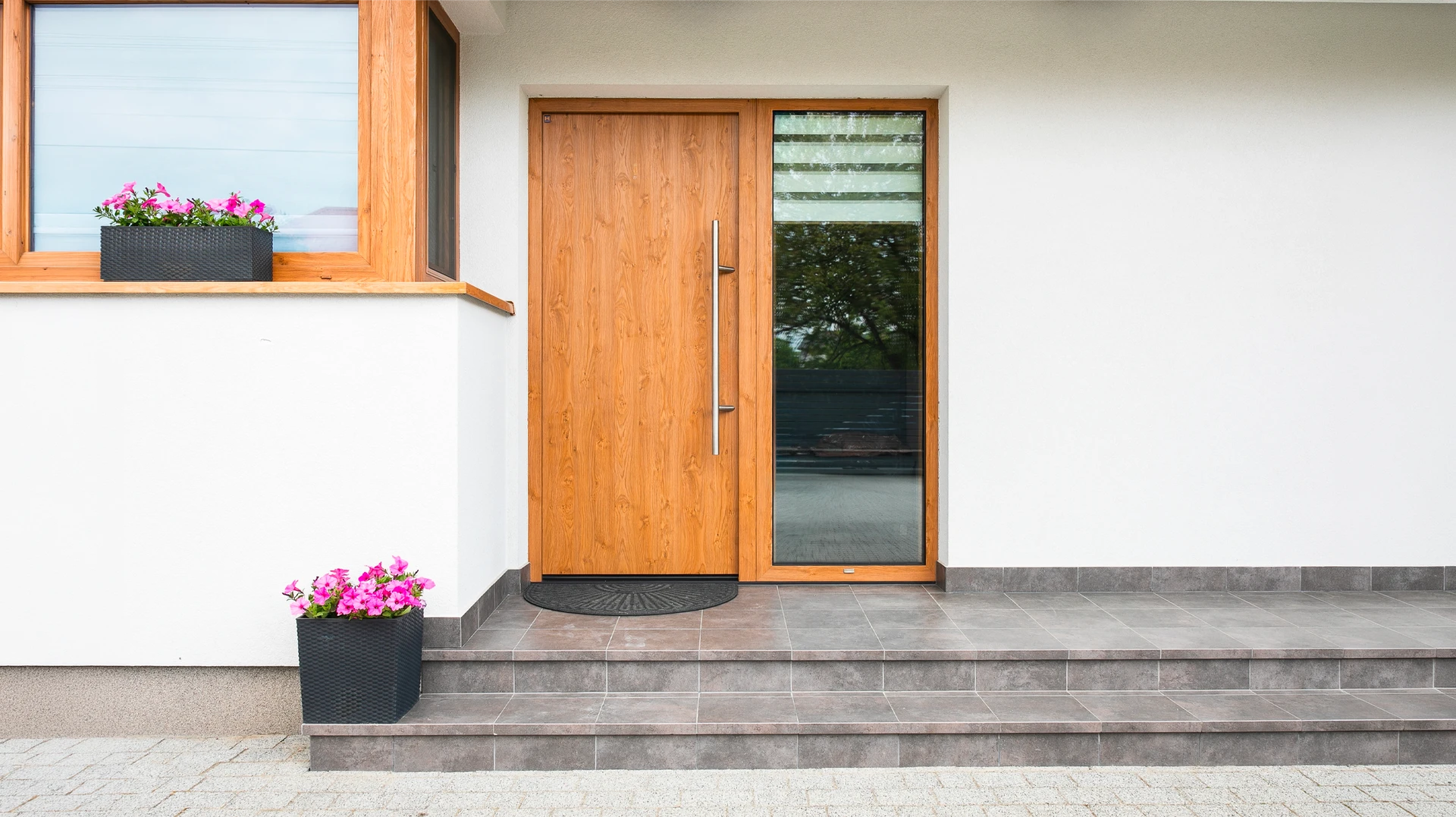 Porte d'entrée en aluminium anthracite RAL 7016 avec trois vitrages décoratifs rectangulaires dépolis encadrés de montants inox brossé, poignée levier inox, serrure multipoints, installée en feuillure dans façade enduite blanche, menuiserie fermée et sécurisée.